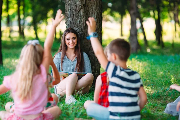 Enfants et éducation, jeune femme au travail comme éducatrice lisant un livre aux garçons et aux filles du parc. — Photo