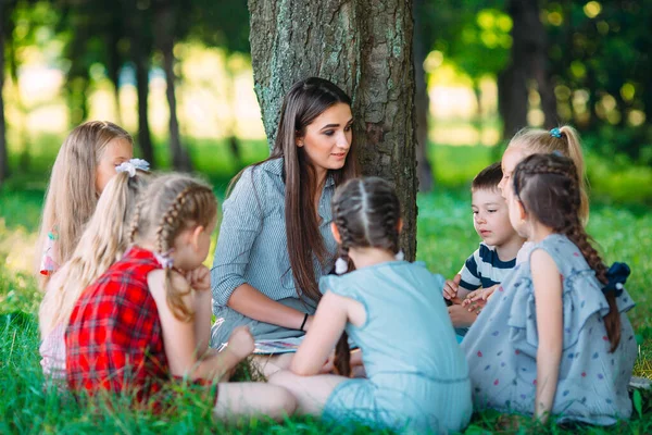 Enfants et éducation, jeune femme au travail comme éducatrice lisant un livre aux garçons et aux filles du parc. — Photo