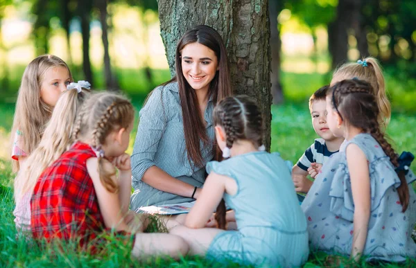 Enfants et éducation, jeune femme au travail comme éducatrice lisant un livre aux garçons et aux filles du parc. — Photo