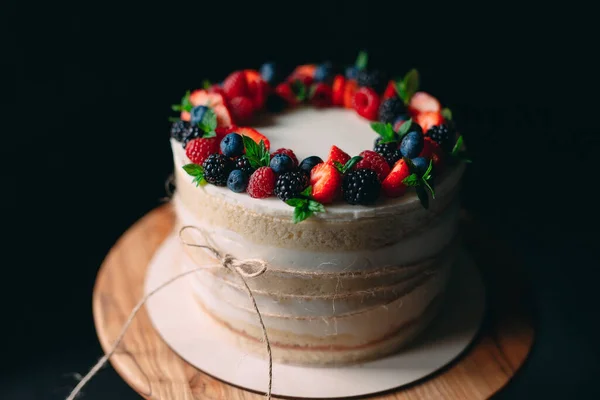 Fruitcake. Taart versierd met bessen op een houten statief op een zwarte achtergrond. — Stockfoto