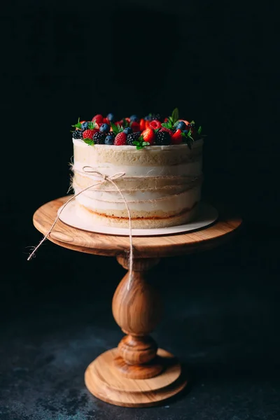 Fruit cake. Cake decorated with berries on a wooden stand on a black background. — Stock Photo, Image