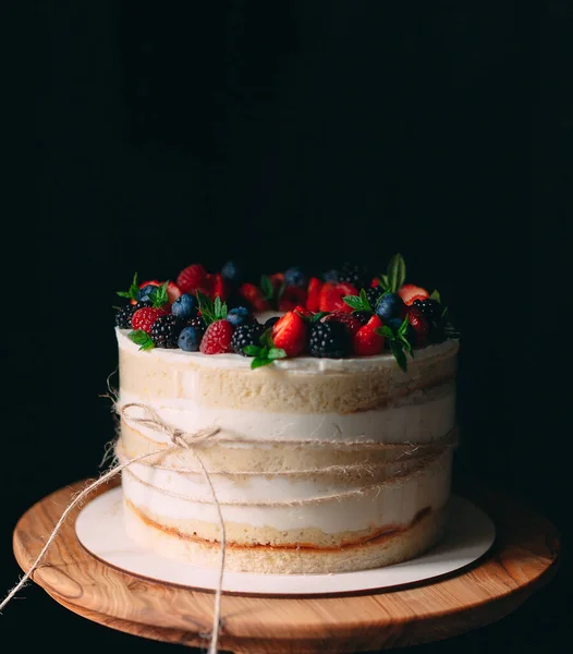 Fruitcake. Taart versierd met bessen op een houten statief op een zwarte achtergrond. — Stockfoto