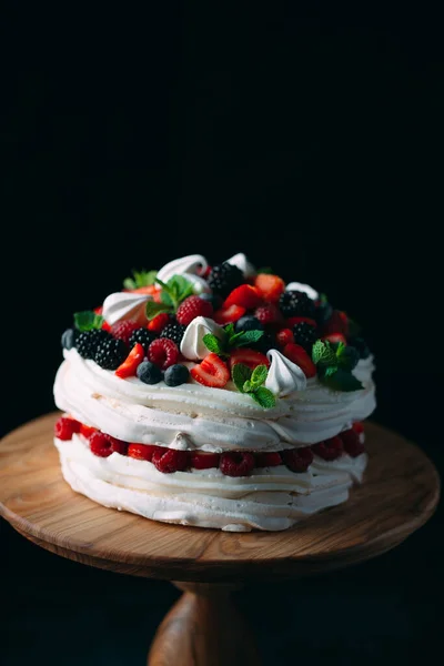 Fruktkaka. Tårta dekorerad med bär på en träställning på en svart bakgrund. — Stockfoto