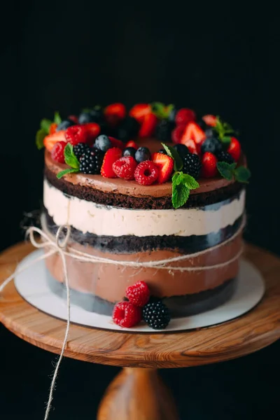 Fruit cake. Cake decorated with berries on a wooden stand on a black background. — Stock Photo, Image