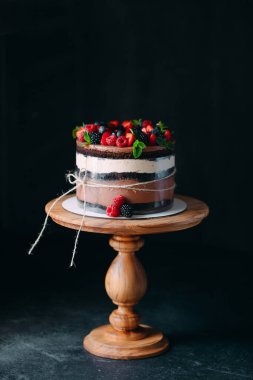 Meyveli kek. Kek, siyah arka plandaki ahşap bir stantta böğürtlenlerle süslenmiş..