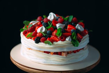 Meyveli kek. Kek, siyah arka plandaki ahşap bir stantta böğürtlenlerle süslenmiş..