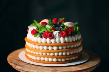 Meyveli kek. Kek, siyah arka plandaki ahşap bir stantta böğürtlenlerle süslenmiş..