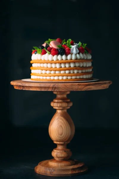 Fruit cake. Cake decorated with berries on a wooden stand on a black background. — Stock Photo, Image