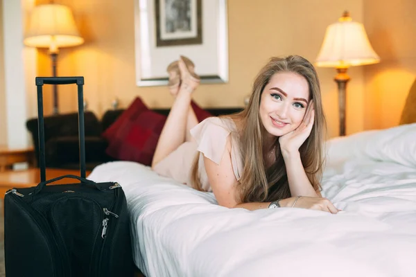 Smiling young businesswoman in bed staring at camera. Hotel room. the girl licks on the bed near the suitcase. — Stock Photo, Image