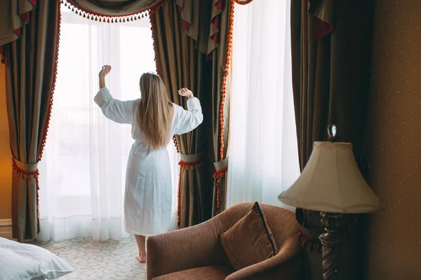 Mujer en albornoz estancia cerca de la ventana en la habitación del hotel. —  Fotos de Stock