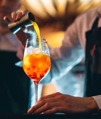 Barmenin eli barın tezgahında kaşıkla taze ve tatlı bir turuncu yaz kokteyli karıştırıyor..