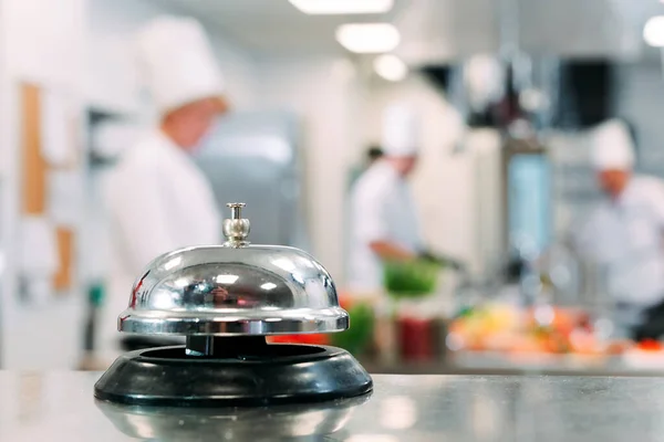 Distribuição de mesa no restaurante. Cozinheiros preparar comida na cozinha contra o fundo de um sino de metal. — Fotografia de Stock