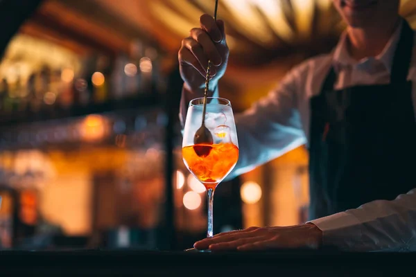 Barman mano revolviendo un cóctel de verano de color naranja fresco y dulce con una cuchara en el mostrador del bar. — Foto de Stock