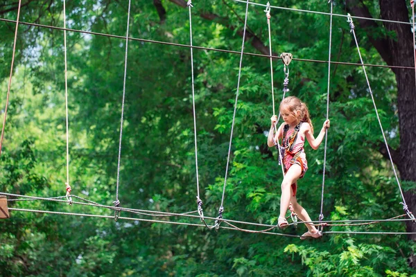 Chica de la escuela feliz disfrutando de la actividad en un parque de aventura de escalada en un día de verano, — Foto de Stock