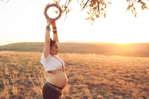 Schwangere beim Yoga auf dem Feld bei Sonnenuntergang. Mädchen mit Traumfänger und Übung — Stockfoto