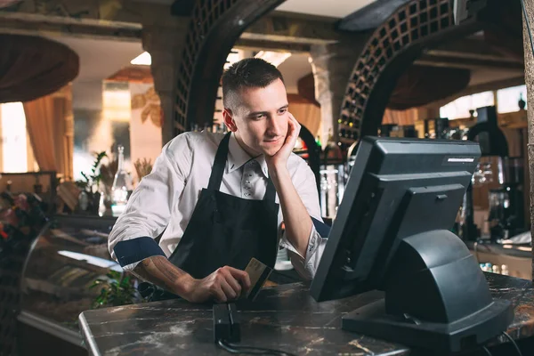 Малый бизнес, люди и концепция сервиса - счастливый человек или официант в фартуке у стойки с банкоматом, работающим в баре — стоковое фото