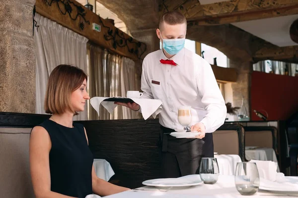 A European-looking waiter in a medical mask serves Latte coffee. — Stock Photo, Image