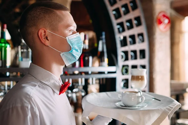 Un cameriere dall'aspetto europeo con una maschera medica serve caffè Latte. — Foto Stock