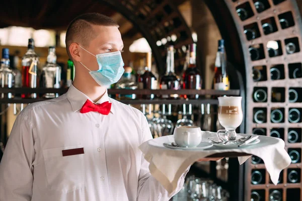 Evropsky vyhlížející číšník v lékařské masce podává kávu Latte.. — Stock fotografie