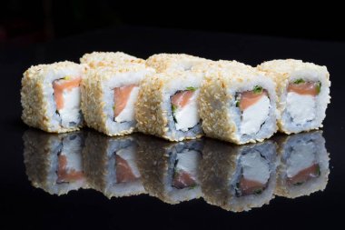 Sushi dürümleri siyah arkaplanda susamlı Chizu sallar..