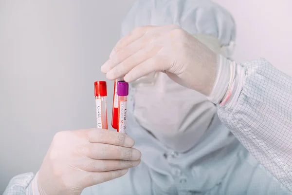 Doctor hombre con máscara antigripal y guantes protectores sosteniendo un tubo de ensayo con una muestra de sangre de coronavirus. Prevenir la gripe Coronavirus. — Foto de Stock