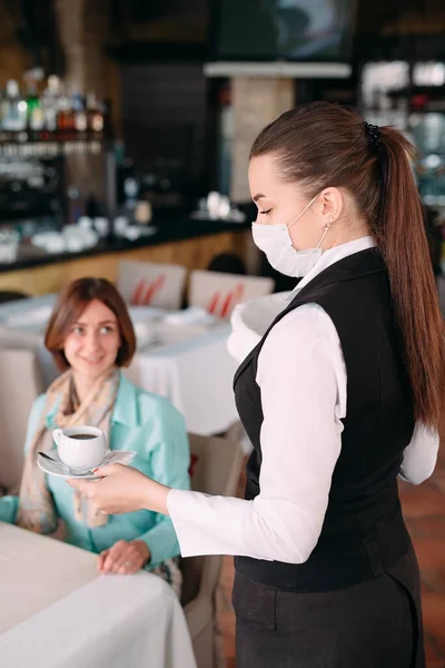 Ένας Ευρωπαίος σερβιτόρος με ιατρική μάσκα σερβίρει καφέ. — Φωτογραφία Αρχείου