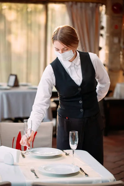 Ένας σερβιτόρος με ιατρική προστατευτική μάσκα σερβίρει το τραπέζι στο εστιατόριο.. — Φωτογραφία Αρχείου