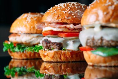 Siyah arka planda sulu sığır etli burgerler.