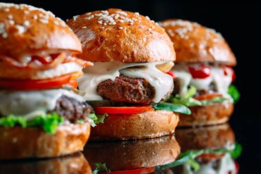 Siyah arka planda sulu sığır etli burgerler.