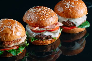 Siyah arka planda sulu sığır etli burgerler.