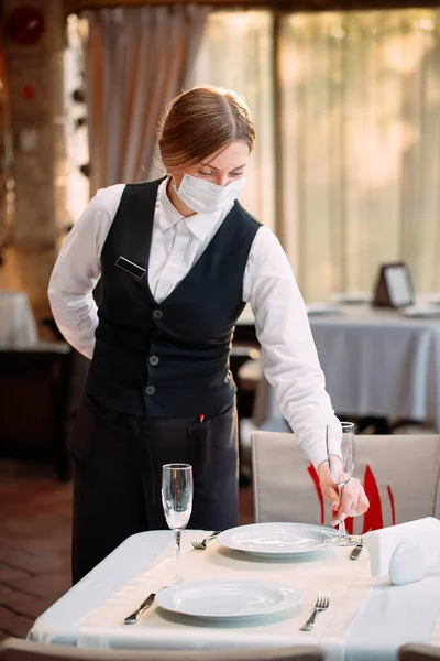 Ένας σερβιτόρος με ιατρική προστατευτική μάσκα σερβίρει το τραπέζι στο εστιατόριο.. — Φωτογραφία Αρχείου