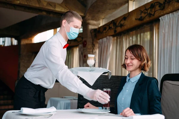 Un camarero de aspecto europeo con máscara médica sirve café Latte. —  Fotos de Stock
