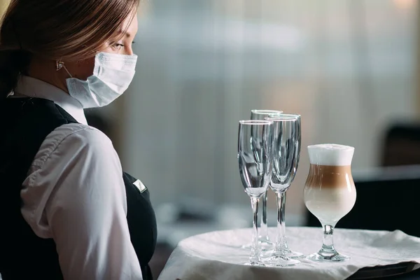 Γυναίκα σερβιτόρος ευρωπαϊκής εμφάνισης με ιατρική μάσκα σερβίρει καφέ Latte. — Φωτογραφία Αρχείου
