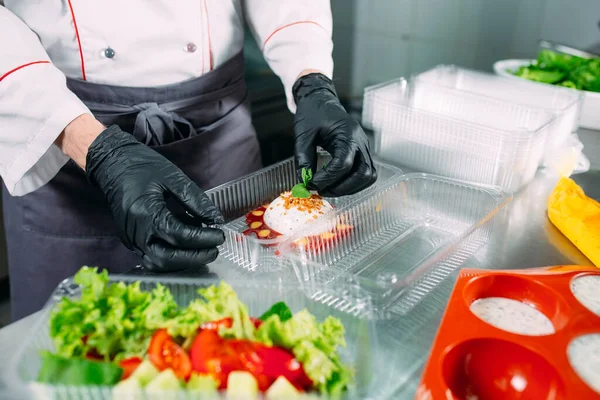 Food delivery in the restaurant. The chef prepares food in the restaurant and packs it in disposable dishes. — Stock Photo, Image