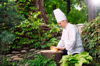 Üniformalı bir restoran şefi ormanda bir kütüğe hamur atıyor..