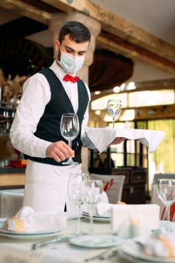 Tıbbi koruyucu maskeli bir garson restorandaki masaya servis yapıyor..