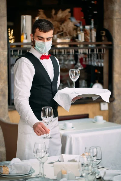 Un cameriere con una maschera protettiva medica serve il tavolo del ristorante. — Foto Stock