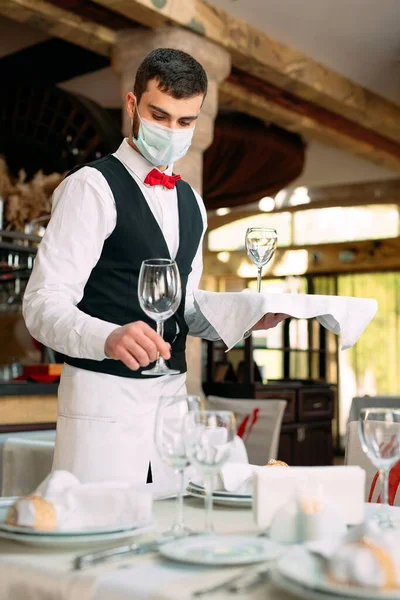 Un cameriere con una maschera protettiva medica serve il tavolo del ristorante. — Foto Stock