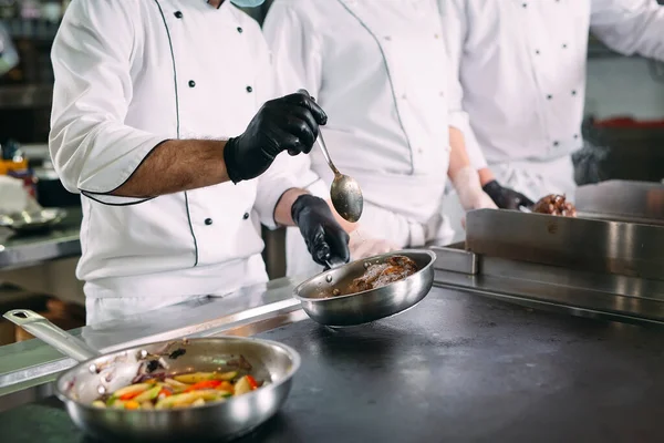 Повара в защитных масках и перчатках готовят еду на кухне ресторана или отеля. — стоковое фото