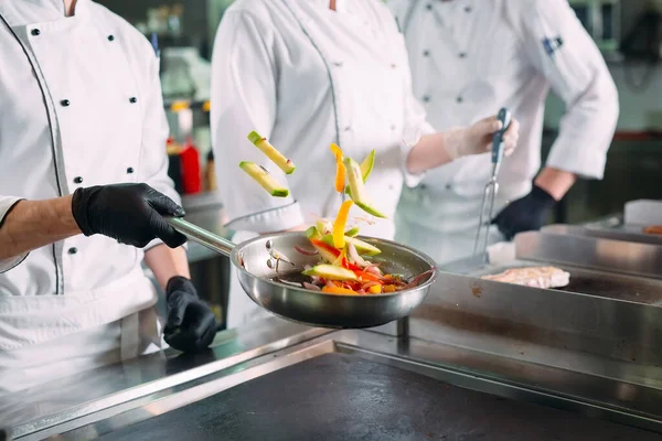 Chefs em máscaras e luvas de proteção preparar alimentos na cozinha de um restaurante ou hotel. — Fotografia de Stock