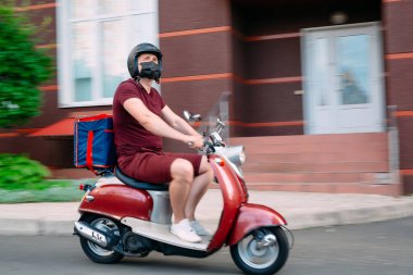 Scooter 'ın üzerinde kırmızı üniformalı teslimatçı çocuk ve hızlı giden izotermal yiyecek kutusu. Kafelerden ve restoranlardan ekspres yemek servisi. Moto scooter 'daki kurye yiyecek getiriyor..
