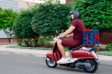 Scooter 'ın üzerinde kırmızı üniformalı teslimatçı çocuk ve hızlı giden izotermal yiyecek kutusu. Kafelerden ve restoranlardan ekspres yemek servisi. Moto scooter 'daki kurye yiyecek getiriyor..
