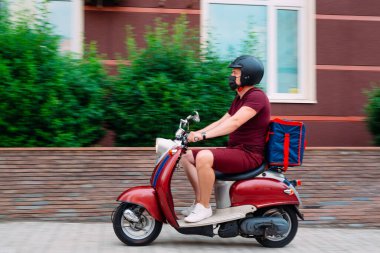 Scooter 'ın üzerinde kırmızı üniformalı teslimatçı çocuk ve hızlı giden izotermal yiyecek kutusu. Kafelerden ve restoranlardan ekspres yemek servisi. Moto scooter 'daki kurye yiyecek getiriyor..