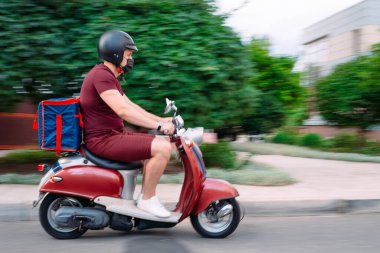 Scooter 'ın üzerinde kırmızı üniformalı teslimatçı çocuk ve hızlı giden izotermal yiyecek kutusu. Kafelerden ve restoranlardan ekspres yemek servisi. Moto scooter 'daki kurye yiyecek getiriyor..