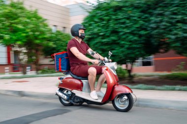 Scooter 'ın üzerinde kırmızı üniformalı teslimatçı çocuk ve hızlı giden izotermal yiyecek kutusu. Kafelerden ve restoranlardan ekspres yemek servisi. Moto scooter 'daki kurye yiyecek getiriyor..