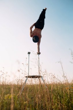Atletik yapılı bir adam gün batımında bir tarlada karmaşık jimnastik egzersizleri yapar..