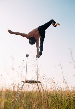 Atletik yapılı bir adam gün batımında bir tarlada karmaşık jimnastik egzersizleri yapar..