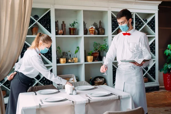 Un cameriere con una maschera protettiva medica serve un tavolo nel ristorante. Dipendenti di un ristorante o di un hotel con maschere protettive. La fine della quarantena. — Foto Stock