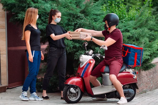 Two womans pick up delivery food box from delivery rider with scooter in front house for social distancing for infection risk.