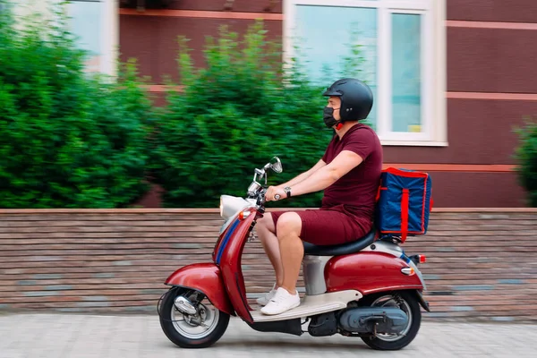 Garoto de entrega vestindo uniforme vermelho em scooter com caixa de comida isotérmica dirigindo rápido. Serviço de entrega de comida expresso de cafés e restaurantes. Correio na moto scooter entrega de alimentos. — Fotografia de Stock